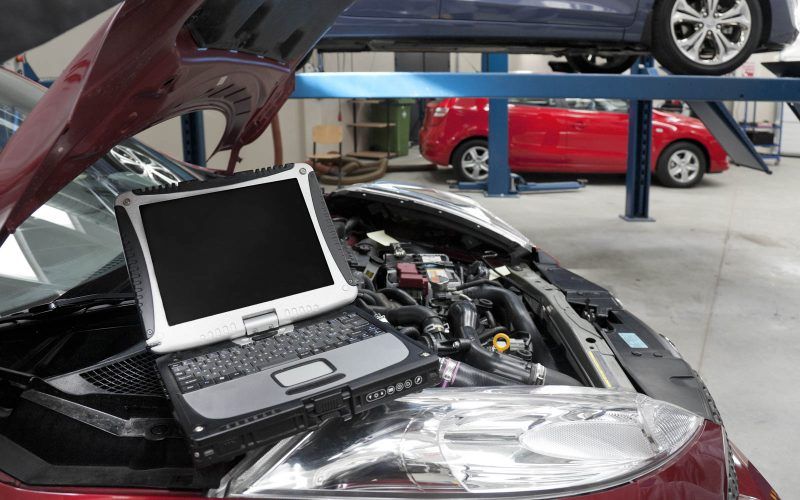 Car in a workshop and a computer running diagnostics on the engine.